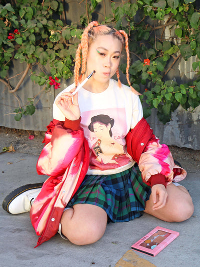 Model wearing a beige t-shirt with a geisha putting on makeup on it.