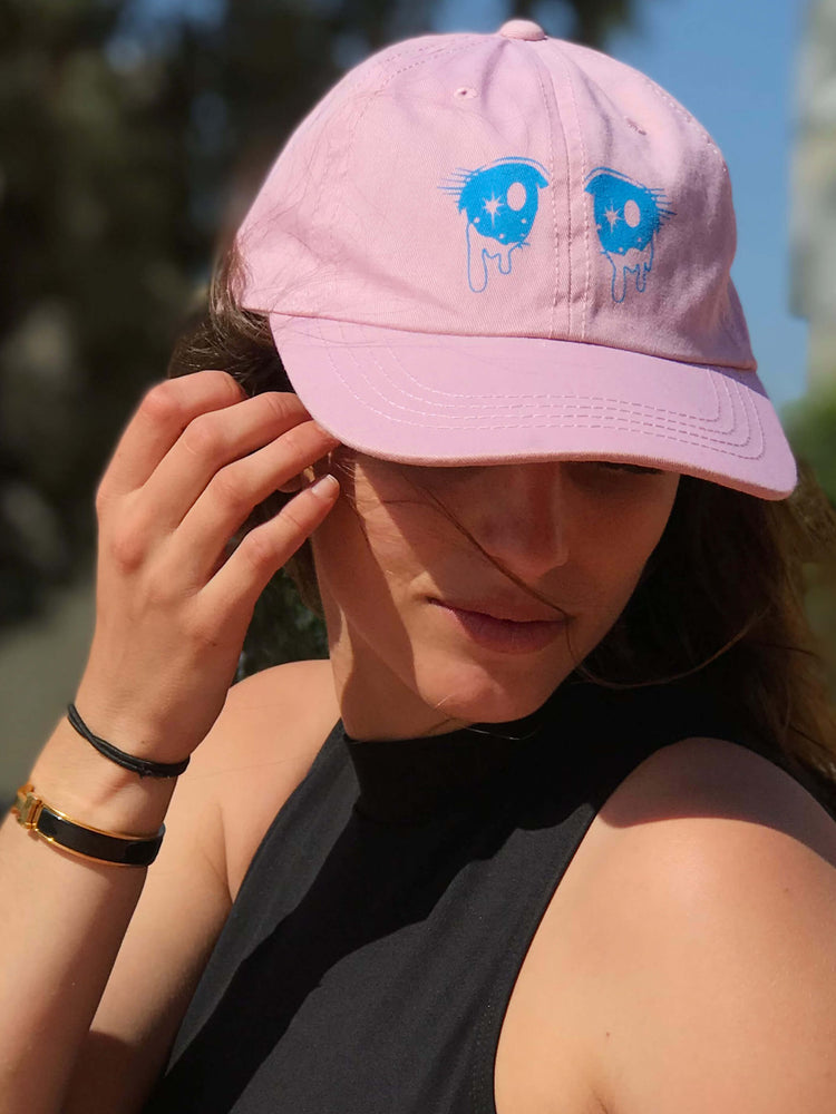 A model wearing a pink dad cap with crying anime eyes on it.
