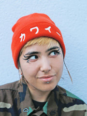 Model wearing an orange beanie that reads kawaii meaning cute in Japanese.