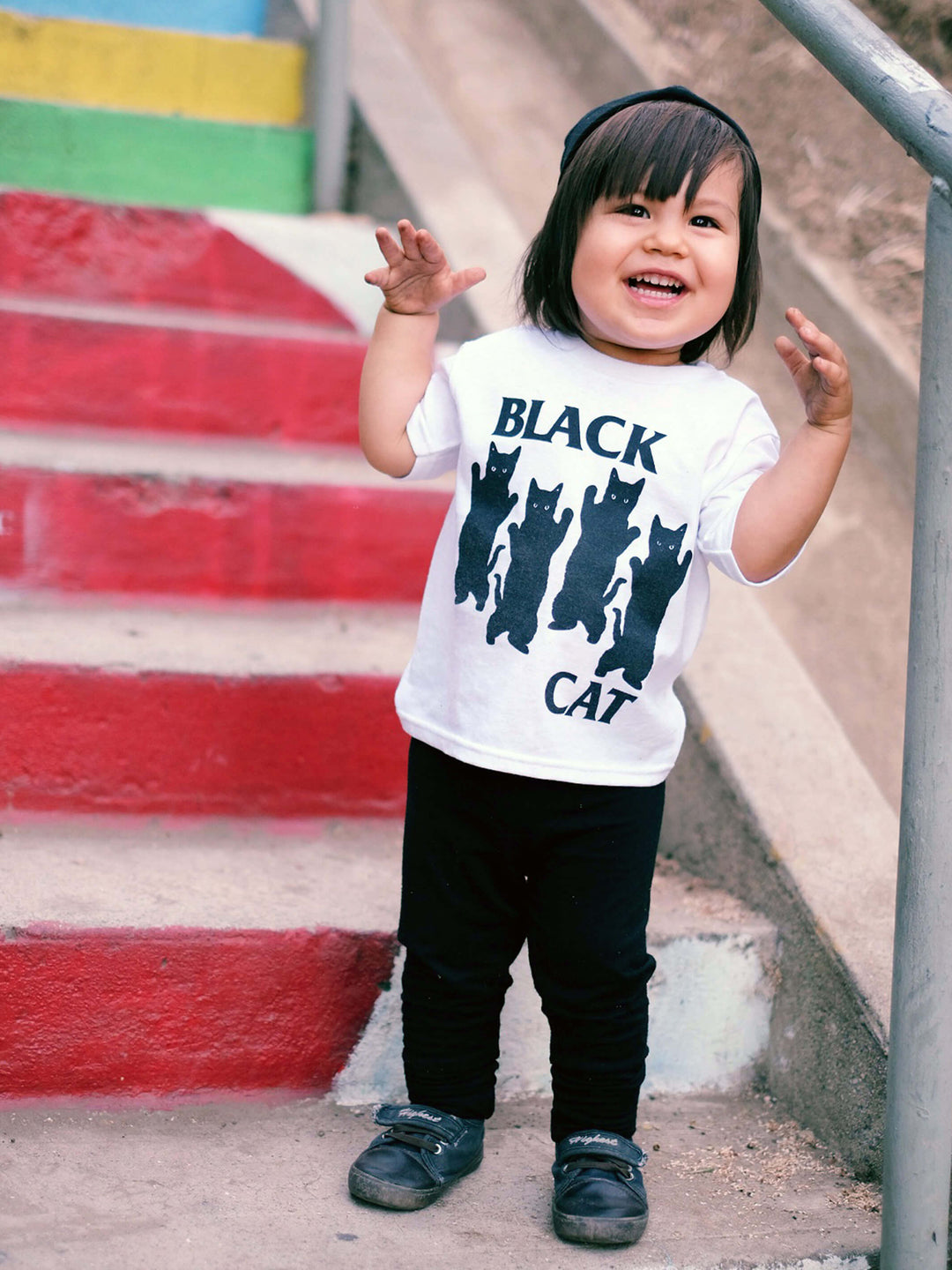 A model wearing a white kid's tee with black cats parodying Black Flag on it.