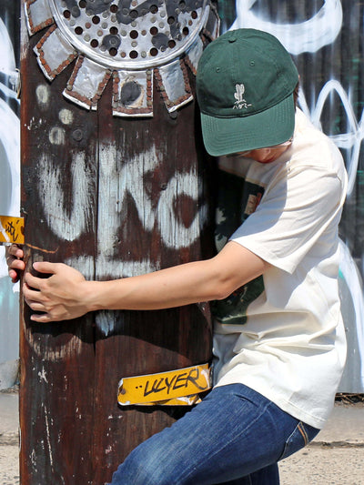 Green baseball cap with an embroidered cactus that reads 'hug me' in Japanese.