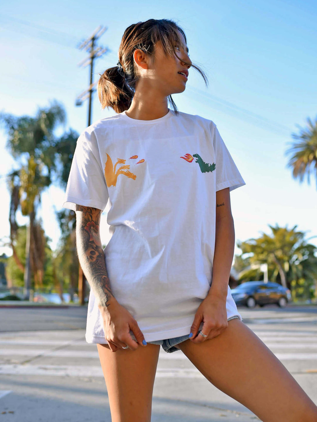 A model wearing a white tee with two kaijus Godzilla and King Ghidorah battling on it.